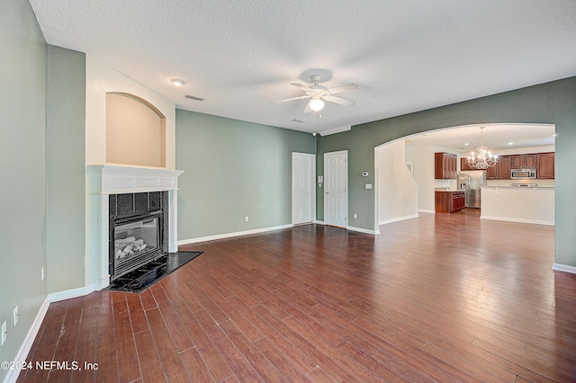 unfurnished living room featuring dark wood-style floors, a fireplace, visible vents, a textured ceiling, and ceiling fan with notable chandelier