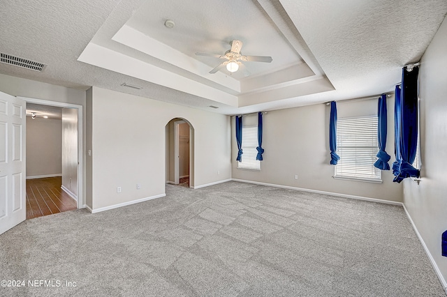 carpeted empty room featuring a textured ceiling, ceiling fan, and a raised ceiling