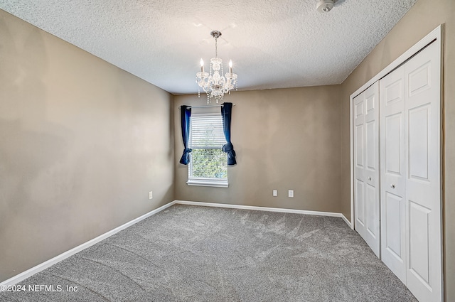 unfurnished bedroom featuring a textured ceiling, a chandelier, a closet, and carpet floors