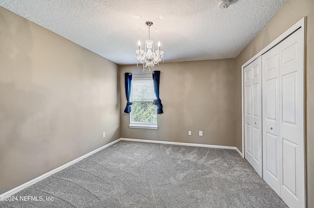 unfurnished bedroom with carpet, a closet, a textured ceiling, a chandelier, and baseboards