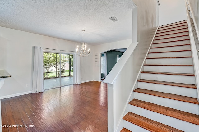 staircase with baseboards, visible vents, hardwood / wood-style flooring, an inviting chandelier, and a textured ceiling