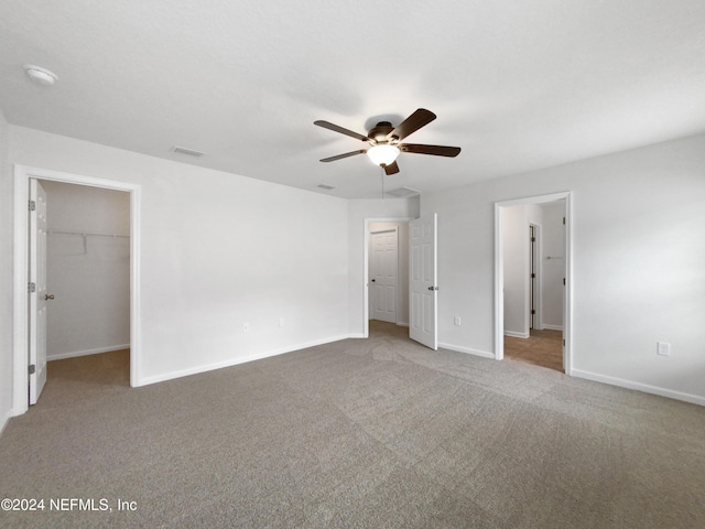 unfurnished bedroom featuring a spacious closet, light colored carpet, and ceiling fan