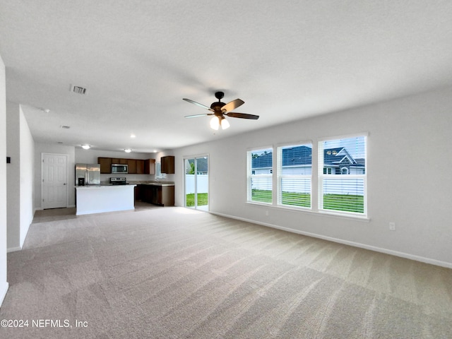 unfurnished living room featuring ceiling fan, light colored carpet, and a textured ceiling