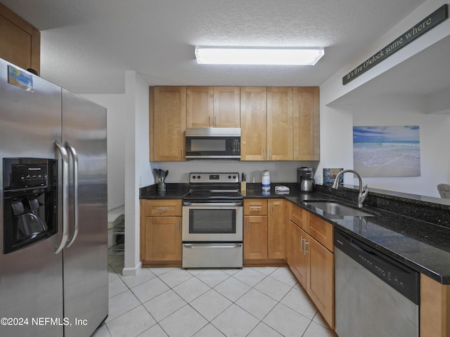 kitchen with dark stone counters, sink, appliances with stainless steel finishes, a textured ceiling, and light tile patterned floors