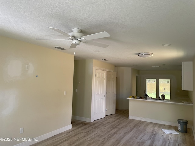 1058 W 17th St, Jacksonville, FL 32209 - unfurnished living room with visible vents, light wood-style floors, baseboards, ceiling fan, and a textured ceiling