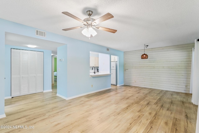 unfurnished living room with baseboards, visible vents, light wood finished floors, ceiling fan, and a textured ceiling