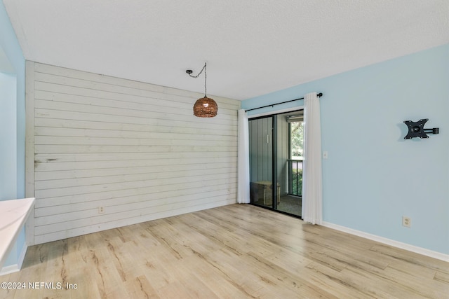 spare room with wood walls, a textured ceiling, baseboards, and wood finished floors