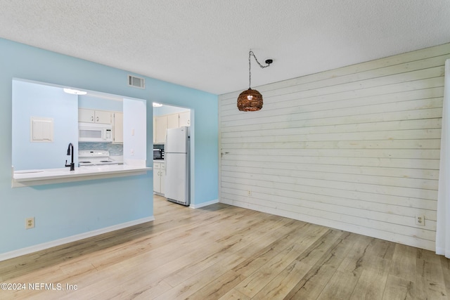 unfurnished dining area with a textured ceiling, wooden walls, visible vents, and light wood-type flooring