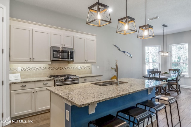 kitchen featuring a center island with sink, stainless steel appliances, decorative light fixtures, white cabinets, and a breakfast bar area