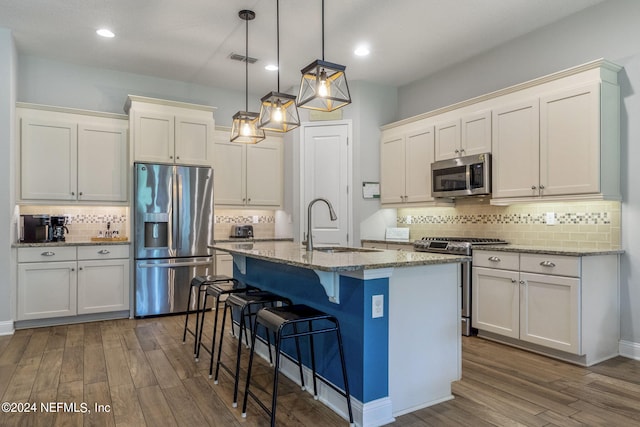 kitchen featuring a center island with sink, light stone counters, decorative light fixtures, stainless steel appliances, and white cabinets