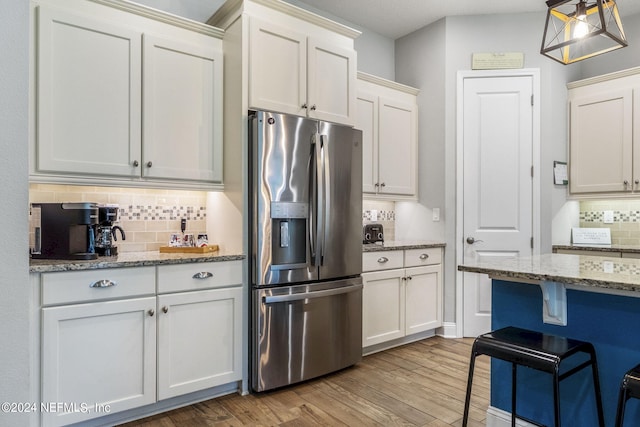 kitchen with white cabinets, pendant lighting, light stone counters, and stainless steel fridge with ice dispenser