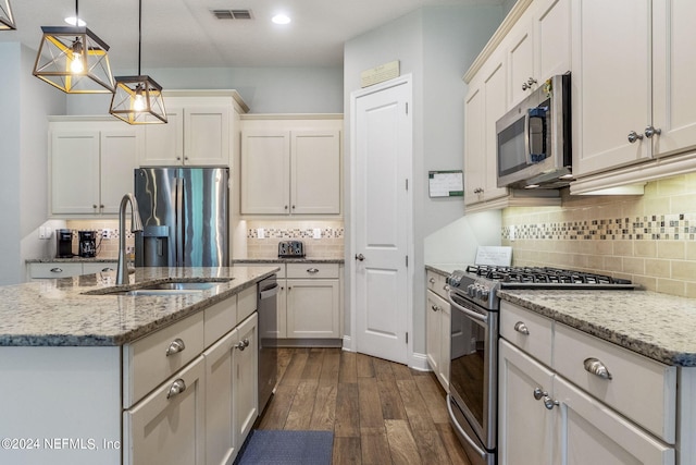 kitchen with a center island with sink, sink, light stone counters, decorative light fixtures, and stainless steel appliances