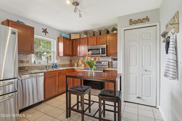 kitchen featuring appliances with stainless steel finishes, light tile patterned floors, decorative backsplash, and light stone counters