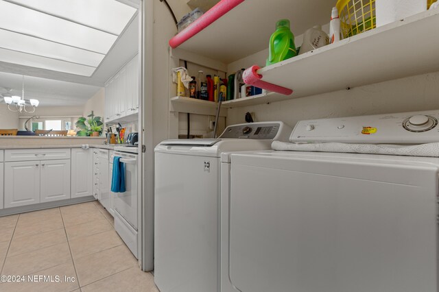 clothes washing area featuring washer and dryer, light tile patterned floors, and a notable chandelier