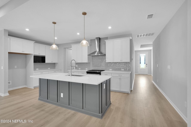 kitchen with white cabinets, sink, a center island with sink, and wall chimney range hood