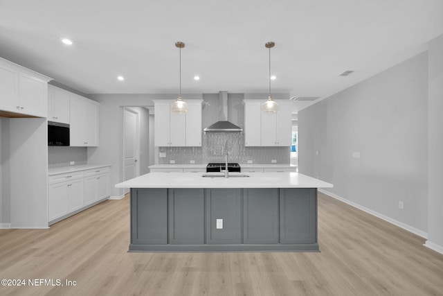 kitchen featuring pendant lighting, white cabinets, light hardwood / wood-style floors, a center island with sink, and wall chimney exhaust hood