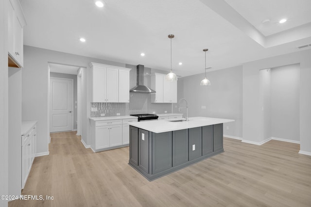 kitchen with white cabinets, a kitchen island with sink, hanging light fixtures, and wall chimney range hood