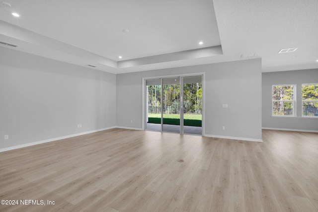 unfurnished room featuring a wealth of natural light, light hardwood / wood-style floors, and a tray ceiling