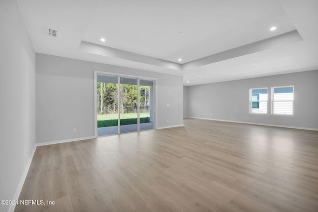 empty room featuring plenty of natural light, a tray ceiling, and light wood-type flooring