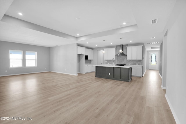 kitchen with pendant lighting, a center island with sink, light wood-type flooring, and wall chimney exhaust hood