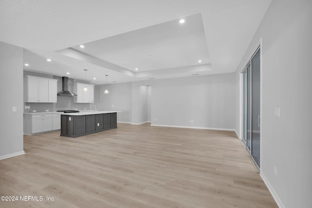 kitchen featuring a raised ceiling, white cabinetry, a kitchen island with sink, and wall chimney exhaust hood