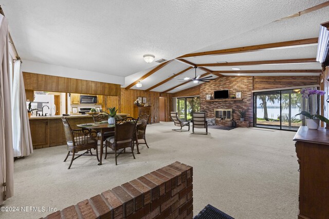 dining area featuring ceiling fan, light carpet, a textured ceiling, wooden walls, and a fireplace