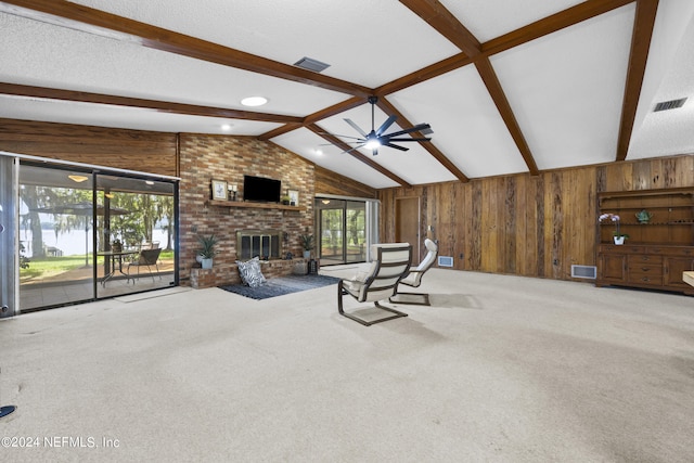 carpeted living room with wooden walls, lofted ceiling with beams, a fireplace, and a wealth of natural light