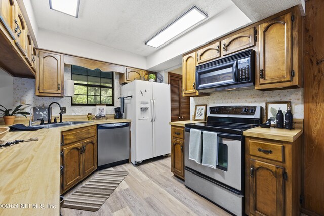 kitchen with appliances with stainless steel finishes, light wood-type flooring, a textured ceiling, and sink