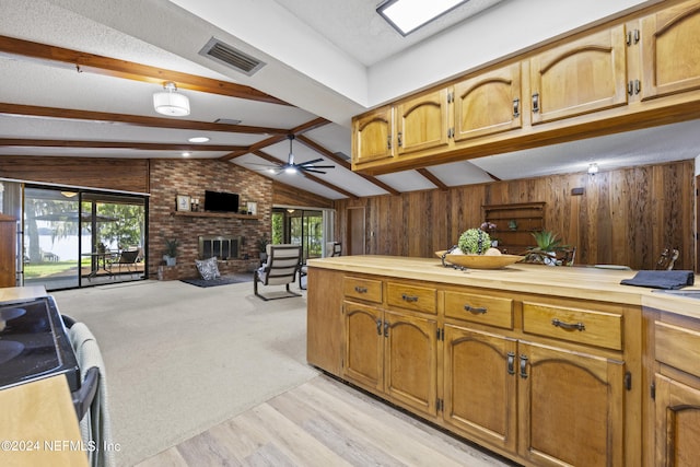 kitchen with wood walls, a fireplace, ceiling fan, and lofted ceiling with beams