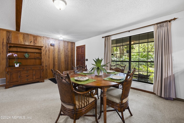 dining space featuring wood walls, light colored carpet, and a textured ceiling