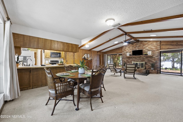 dining room featuring a fireplace, lofted ceiling with beams, light carpet, and a textured ceiling