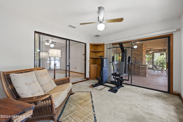 exercise area with a textured ceiling, light colored carpet, and ceiling fan