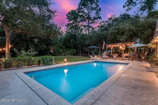 pool at dusk featuring a patio and a lawn