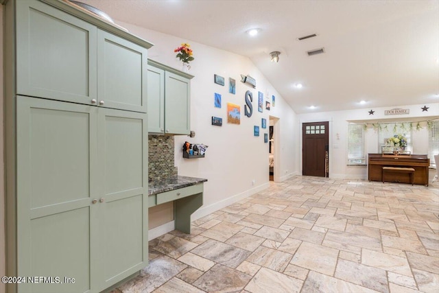 interior space featuring vaulted ceiling, dark stone countertops, green cabinets, and backsplash