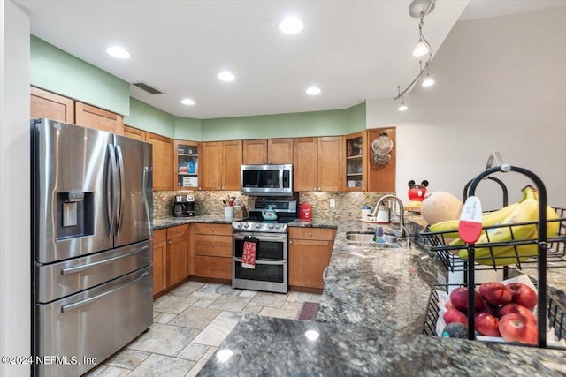 kitchen with tasteful backsplash, appliances with stainless steel finishes, sink, and dark stone countertops