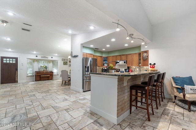 kitchen with vaulted ceiling, stainless steel fridge, a kitchen breakfast bar, decorative backsplash, and kitchen peninsula