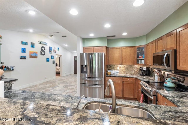 kitchen with lofted ceiling, sink, dark stone countertops, backsplash, and stainless steel appliances