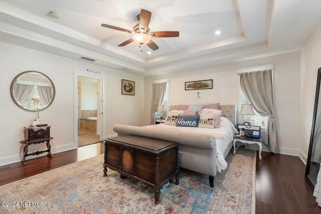 bedroom with dark wood-type flooring, connected bathroom, ceiling fan, and a tray ceiling