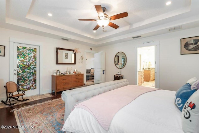 bedroom with dark hardwood / wood-style floors, ceiling fan, ensuite bathroom, and a tray ceiling