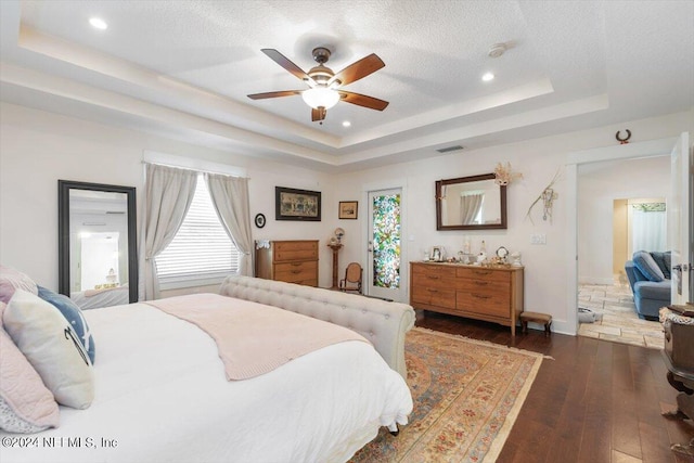 bedroom featuring a raised ceiling, dark hardwood / wood-style floors, a textured ceiling, and multiple windows