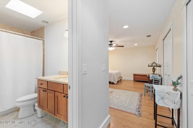 bathroom with toilet, a skylight, vanity, ceiling fan, and hardwood / wood-style floors