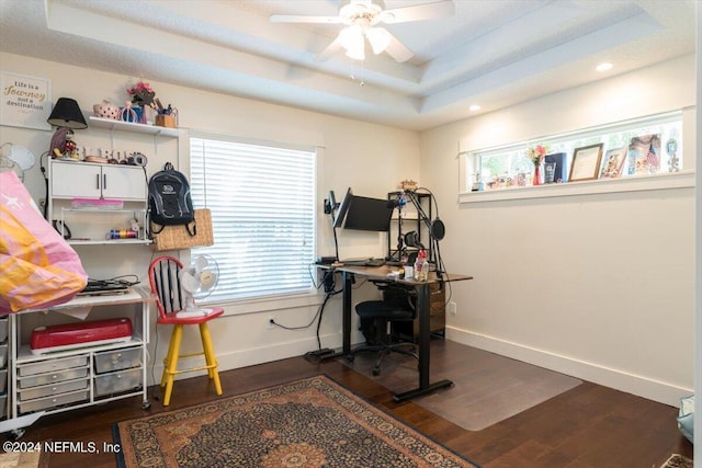 home office with dark wood-type flooring, ceiling fan, a healthy amount of sunlight, and a raised ceiling