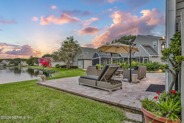 patio terrace at dusk featuring a water view and a lawn