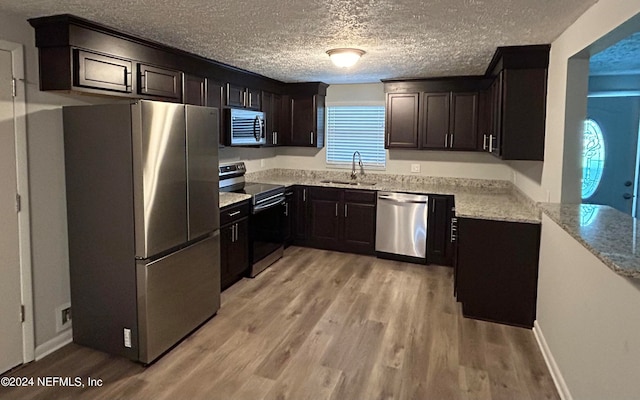 kitchen with a textured ceiling, light hardwood / wood-style flooring, appliances with stainless steel finishes, and light stone counters