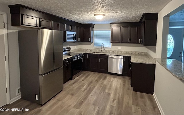 kitchen with appliances with stainless steel finishes, sink, light stone counters, a textured ceiling, and light wood-type flooring