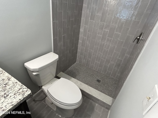 bathroom with tile patterned flooring, vanity, a tile shower, and toilet