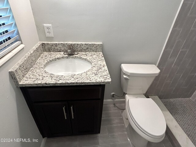 bathroom featuring tile patterned flooring, vanity, tiled shower, and toilet