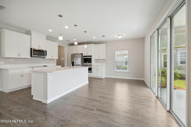 kitchen featuring appliances with stainless steel finishes, a kitchen island with sink, hanging light fixtures, and white cabinets