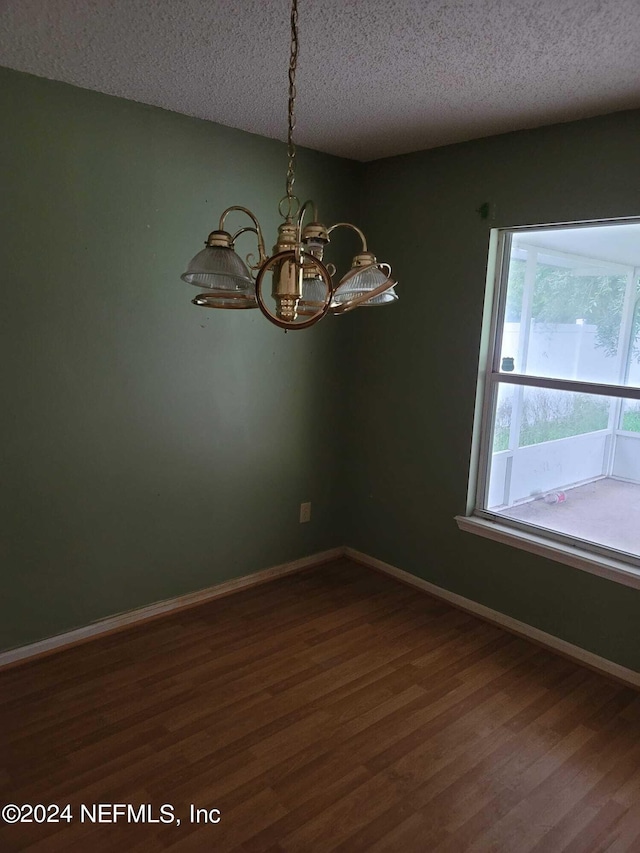 empty room with dark hardwood / wood-style floors, a textured ceiling, and an inviting chandelier