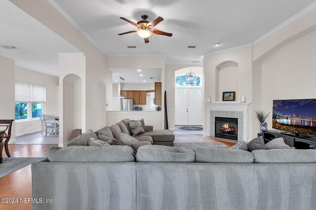 living room with a fireplace, wood-type flooring, crown molding, and ceiling fan